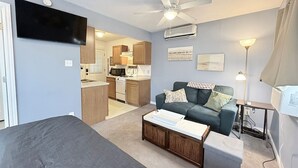 Um espaço de estar compacto com cozinha compacta, sofá, mesa de centro e ventoinha de teto.