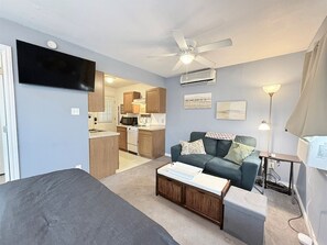 A compact living space with a kitchenette, a sofa, a coffee table, and a ceiling fan. - Eleven South: One - Modern Studio Apartment (Abilene)