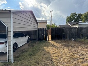 A residential property with a covered garage, a white car parked inside, and a wooden fence surrounding the yard.
