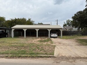 A two-story building with a covered parking area and a grassy lawn.