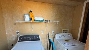 Uma área de lavanderia com duas máquinas de lavar e uma prateleira com produtos de limpeza.