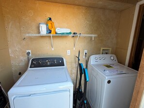 A laundry area with two washing machines and a shelf with cleaning supplies. - Eleven South: One - Modern Studio Apartment (Abilene)