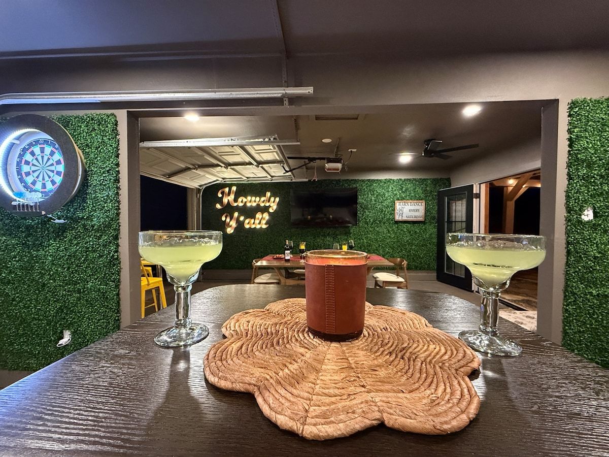 A bar area with a dartboard, a neon sign, and two cocktails on a woven placemat.