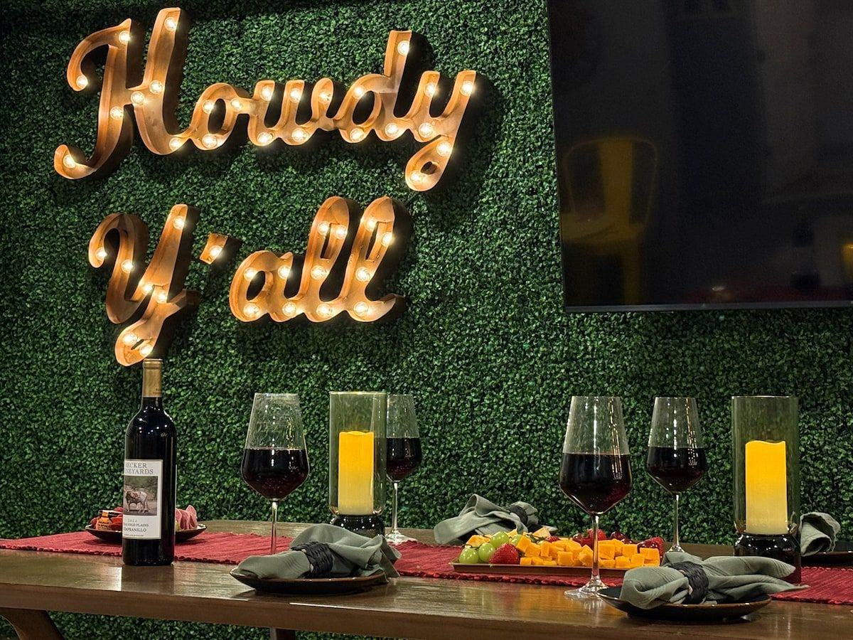 A table with a bottle of wine, glasses, and a candle, set against a backdrop with illuminated text.