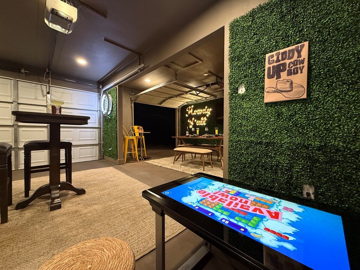 A room with a digital game table, a neon sign, and a green wall with a sign.