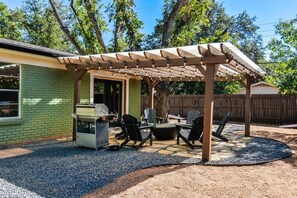 Um pátio com churrasqueira, área de estar ao ar livre e pérgola.