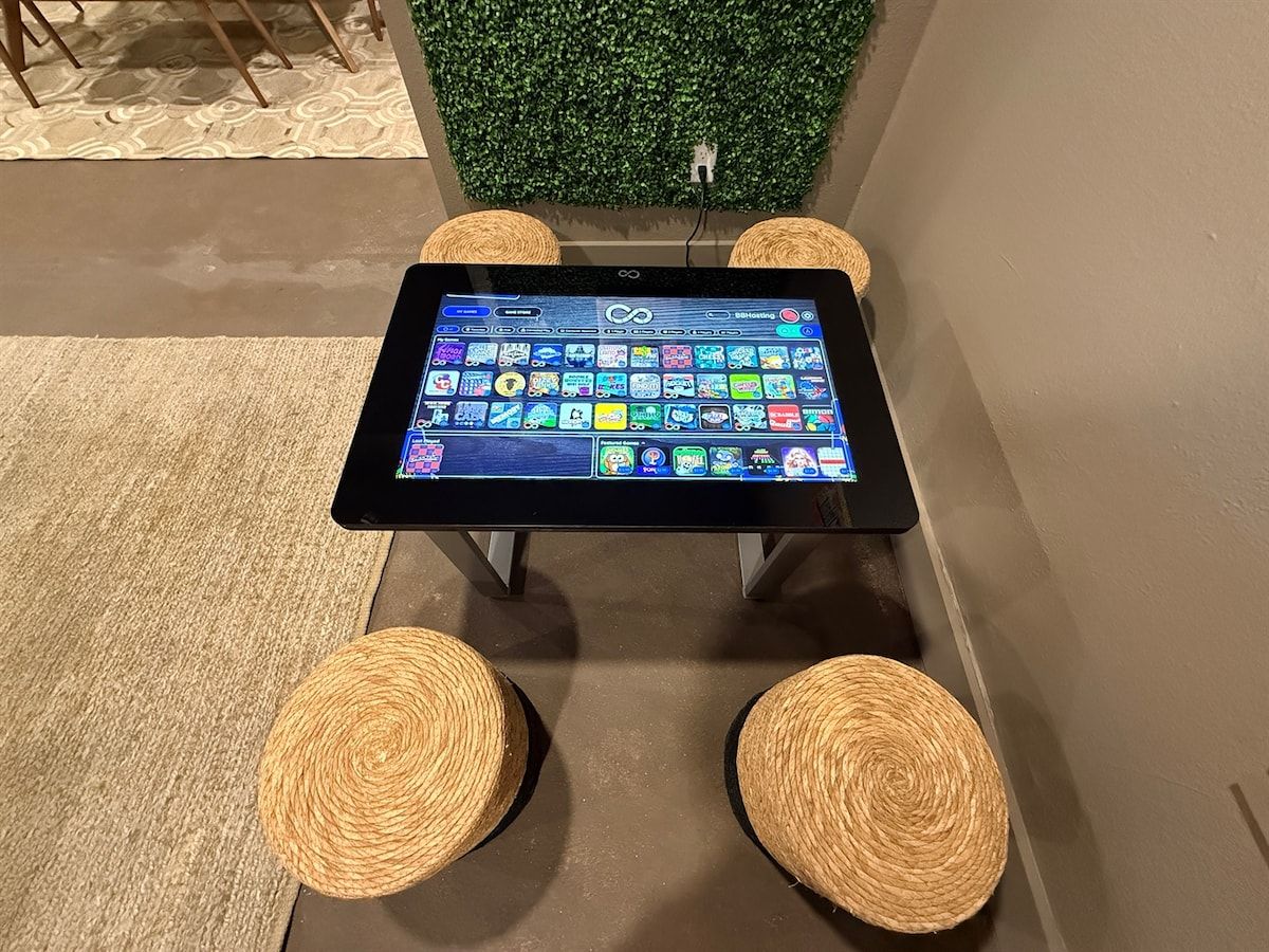 A tablet on a table with four woven stools, a green wall, and a power outlet.