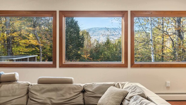 A beige sectional sofa with three windows offering views of autumn foliage and a distant mountain range.