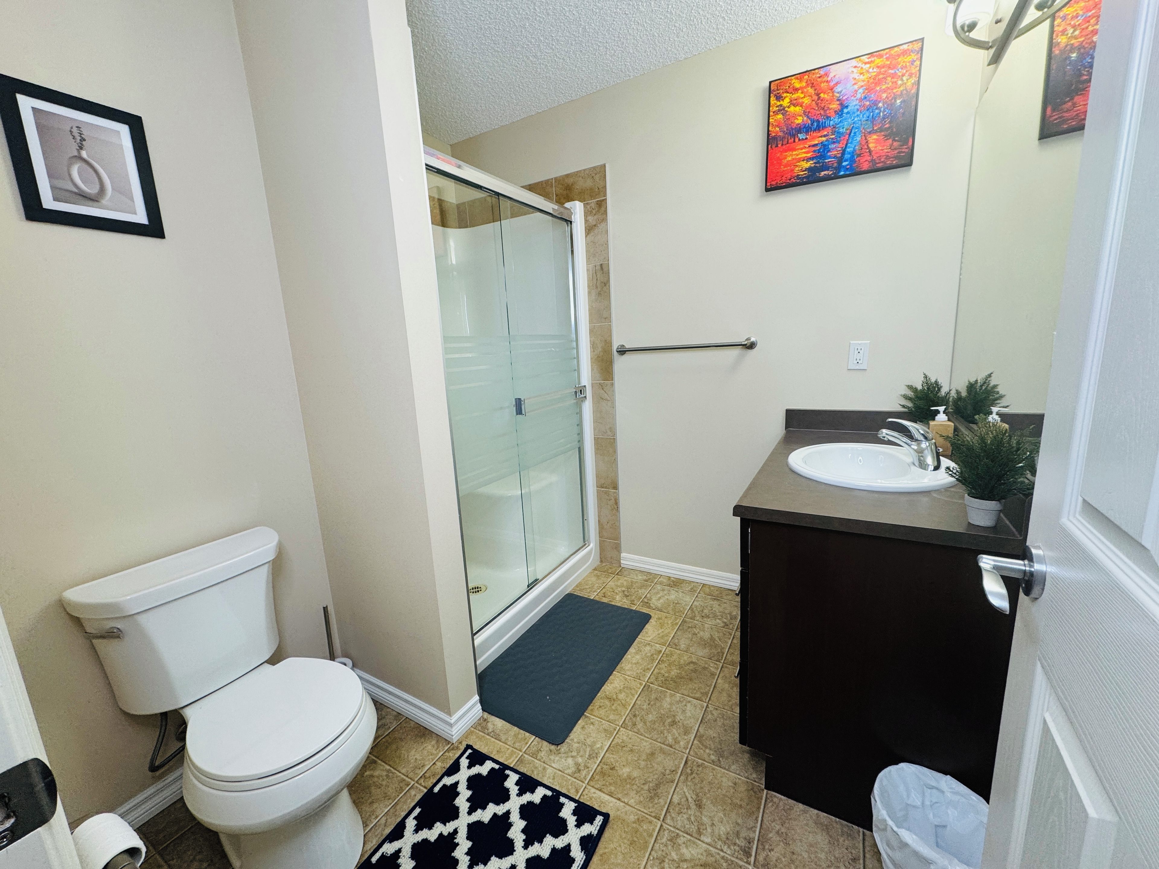 A bathroom with a toilet, a glass shower enclosure, a sink with a mirror, and a small potted plant.