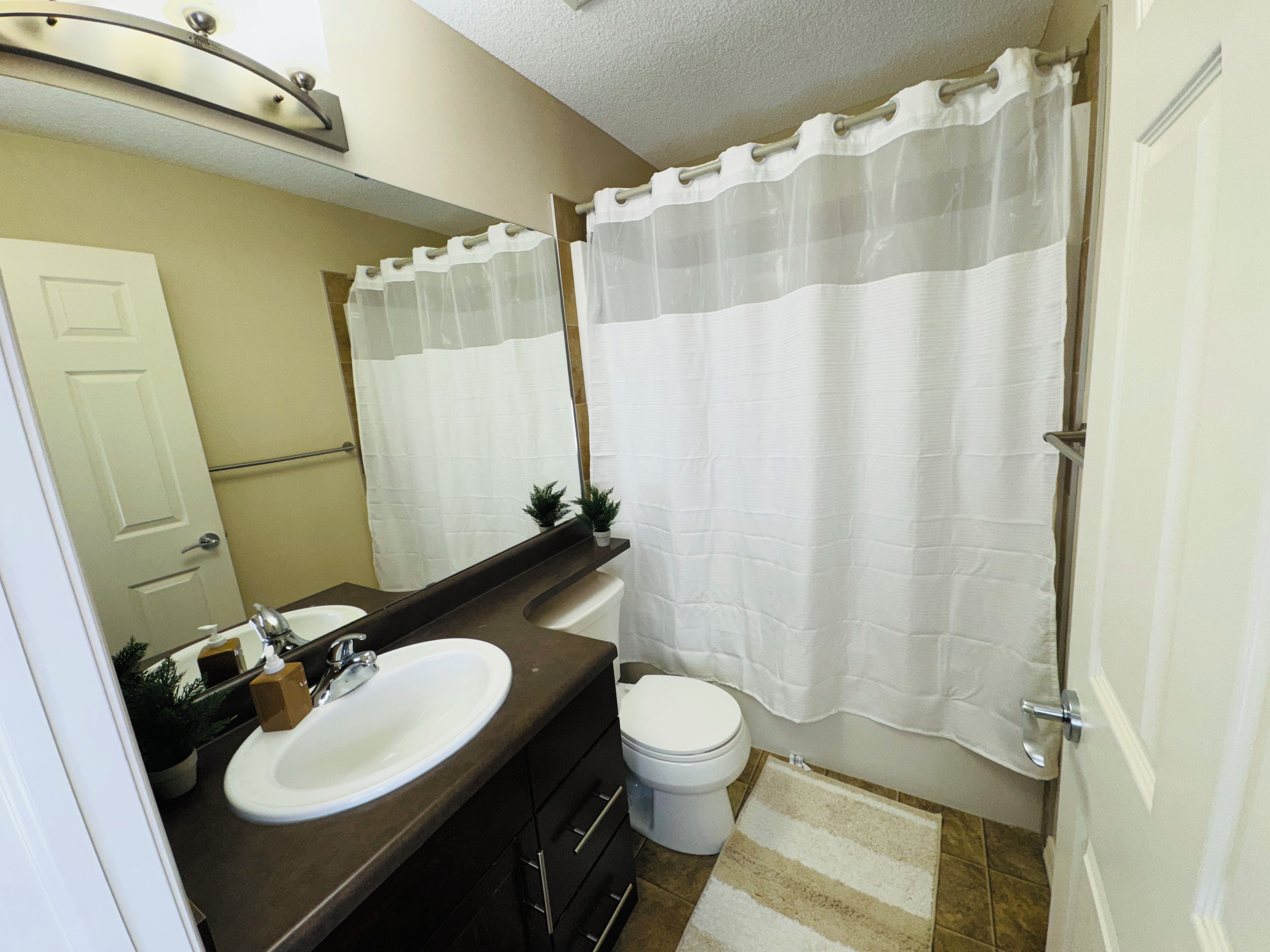 A bathroom with a white sink, a toilet, a mirror, and a shower curtain.