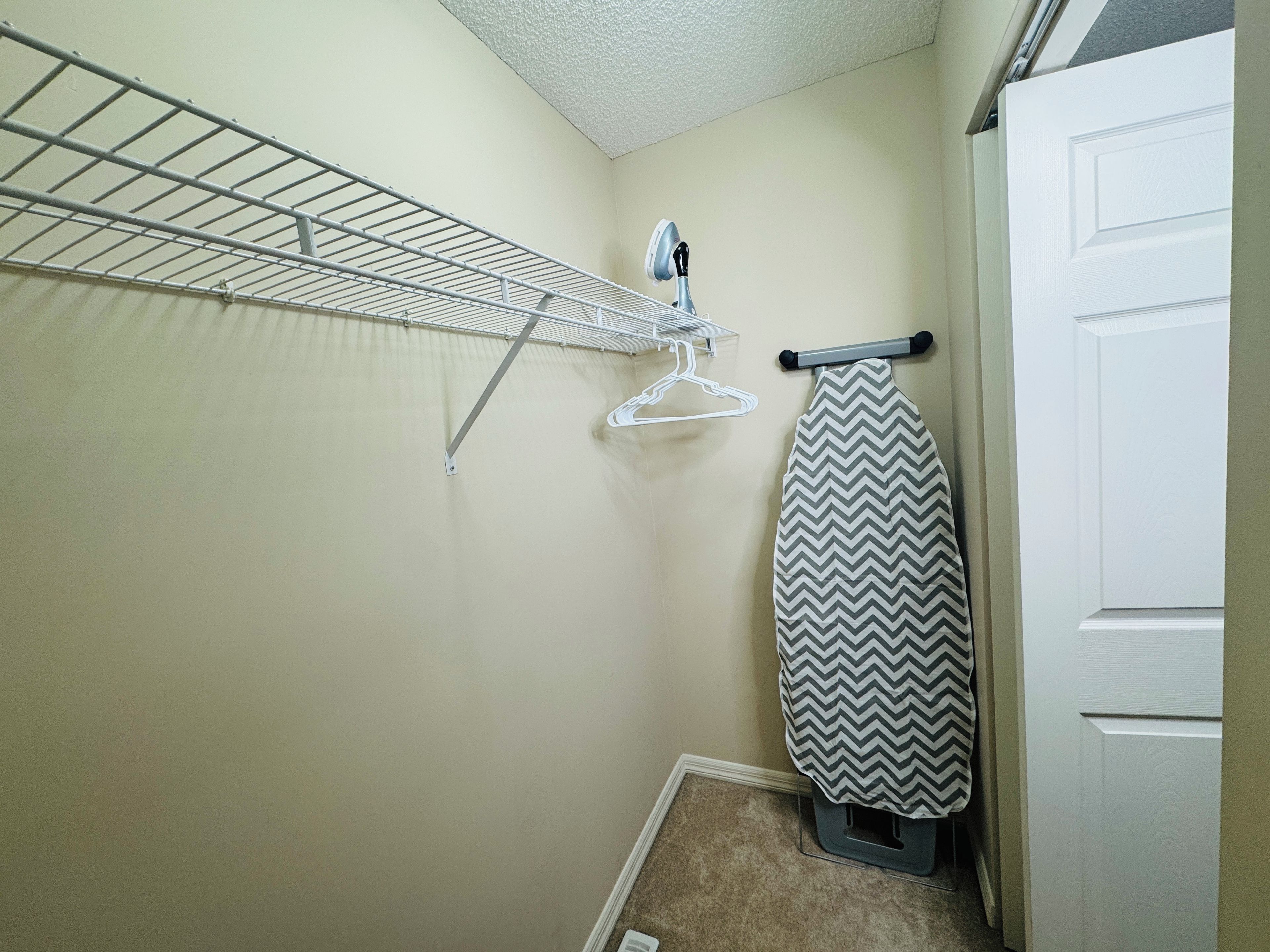 A laundry area with a drying rack, an iron, and a hanging clothes rack.