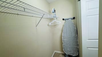 A laundry area with a drying rack, an iron, and a hanging clothes rack.
