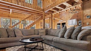 A wooden interior with a large L-shaped sectional sofa, a round coffee table, and a staircase. - Log Cabin by the Lake|Hot Tub, Fire Pit, Games (Blue Ridge)