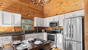 A modern kitchen with white cabinets, stainless steel appliances, and a wooden ceiling. - Log Cabin by the Lake|Hot Tub, Fire Pit, Games (Blue Ridge)