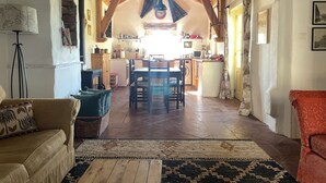 A cozy living room with a sofa, a coffee table, and a rug. There is a kitchen in the background with a dining table and chairs.