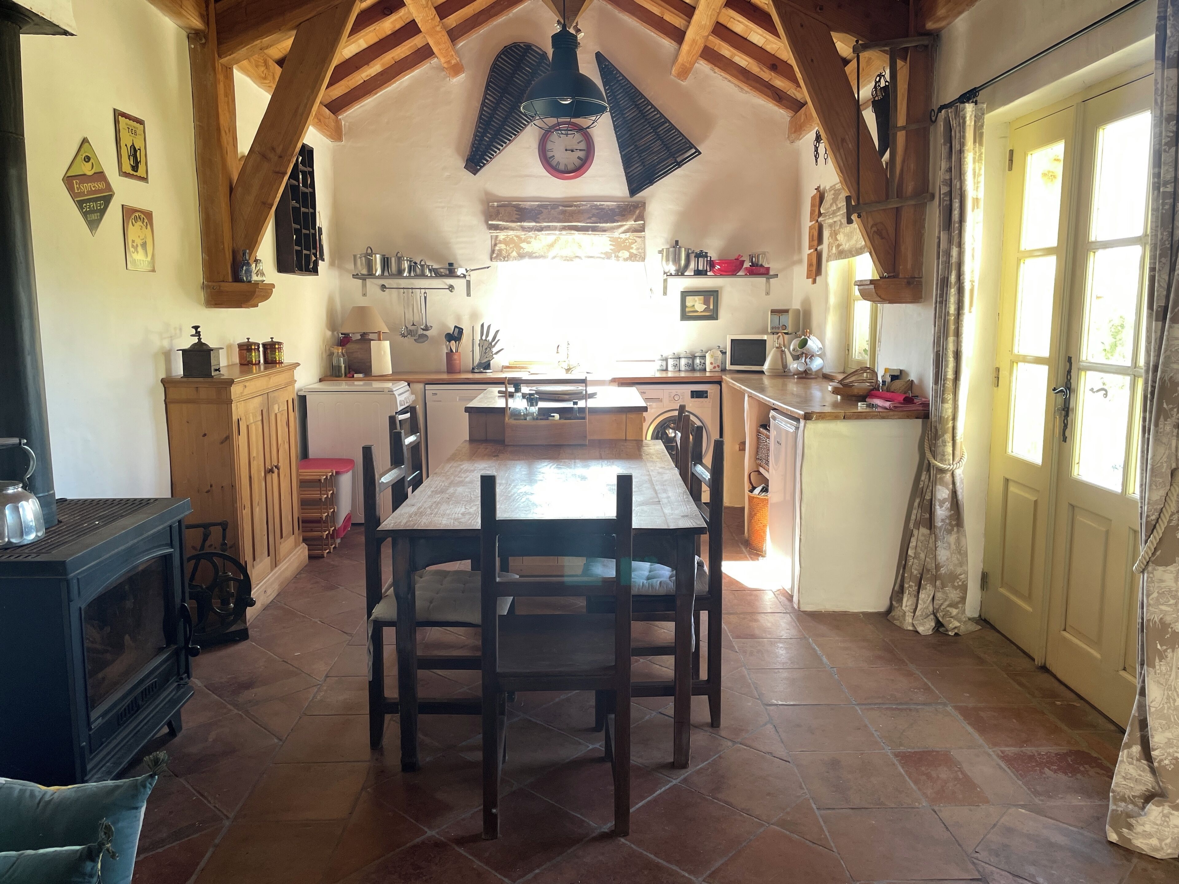 Une cuisine chaleureuse avec des poutres en bois, un îlot central et une table à manger avec des chaises.