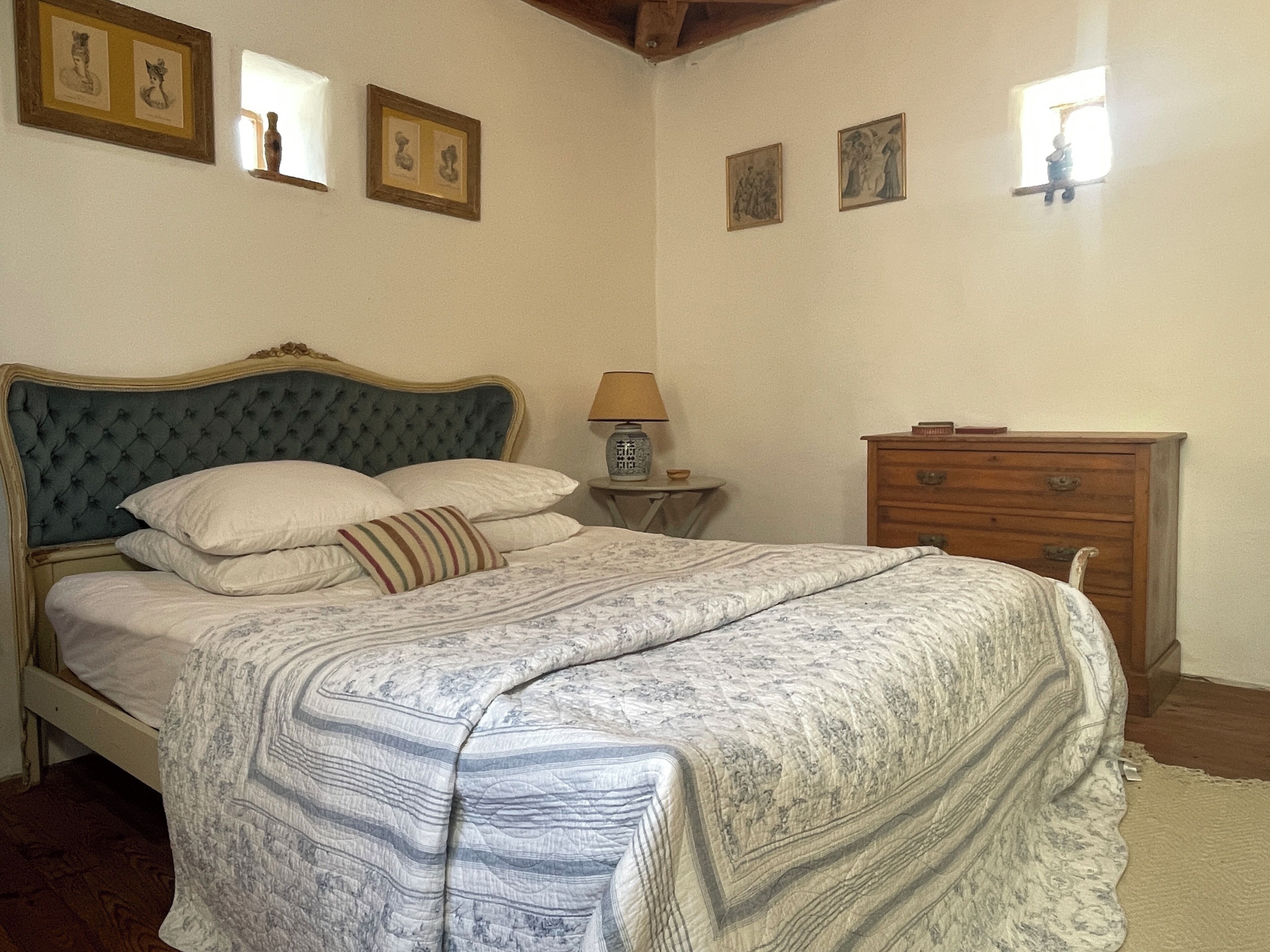 A bedroom with a bed, a wooden dresser, a nightstand, and framed pictures on the wall.