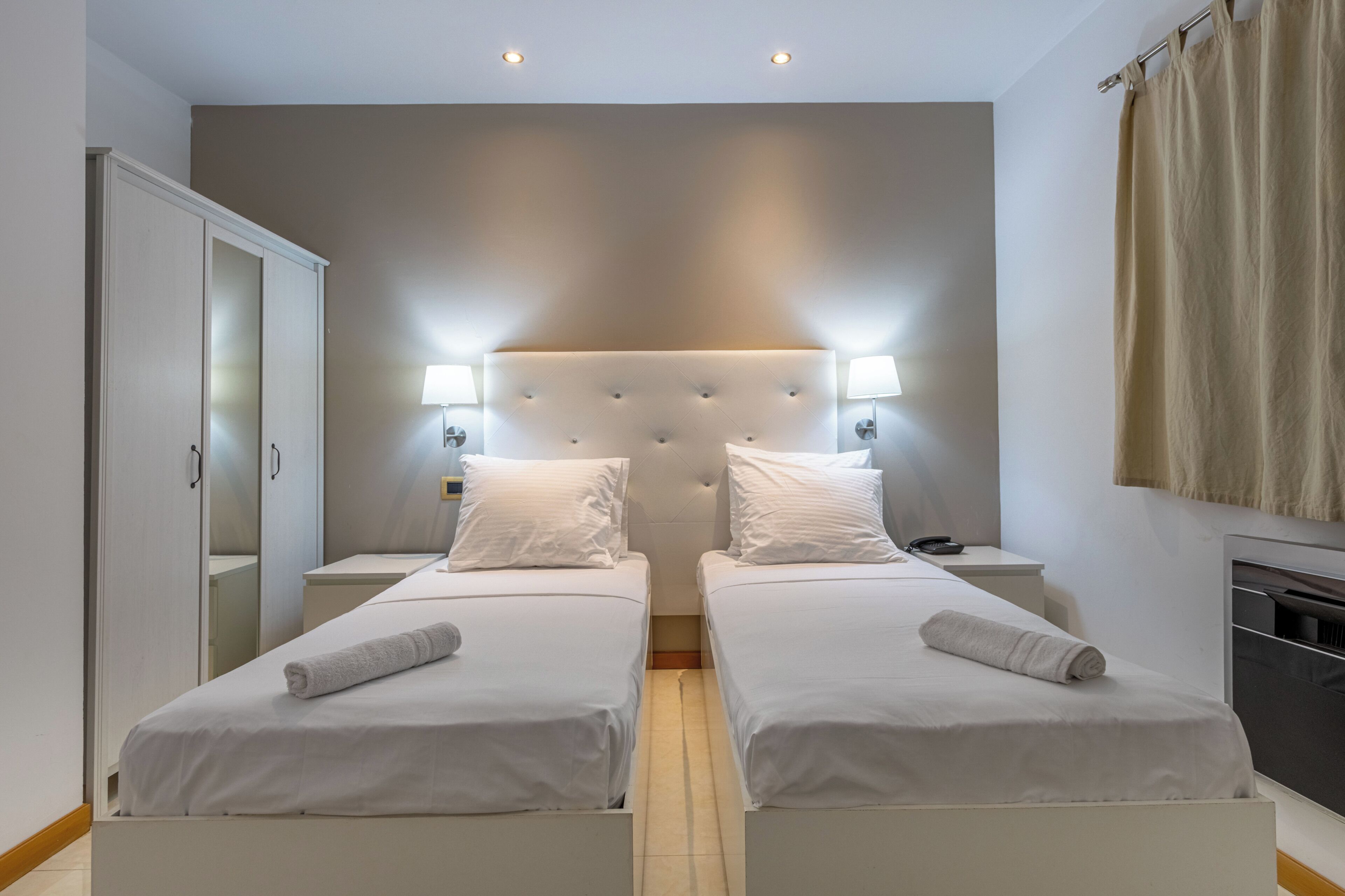 Habitación de hotel con dos camas, un armario, un espejo y un televisor.