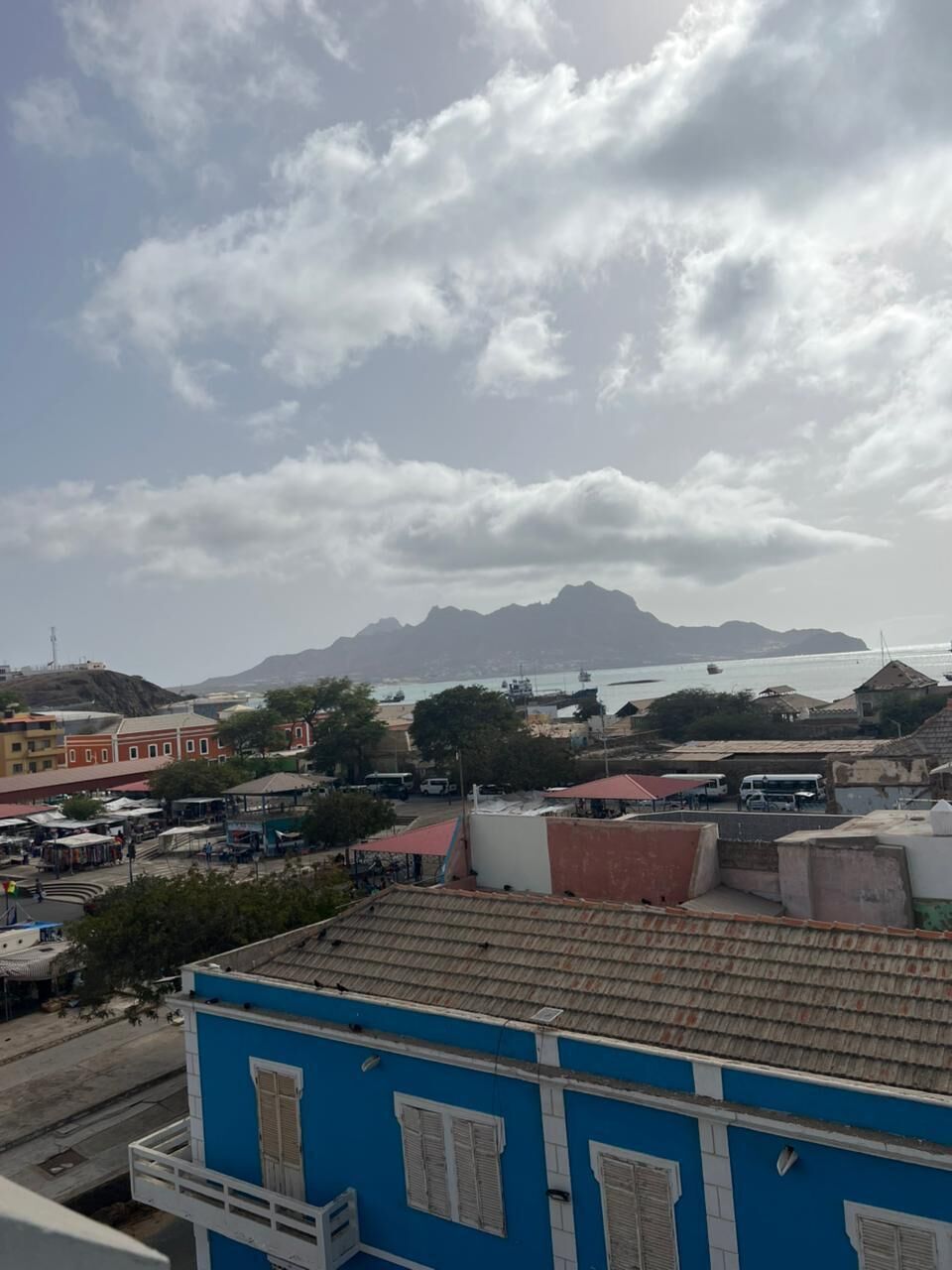 A coastal cityscape with buildings, a clear sky, and distant mountains.