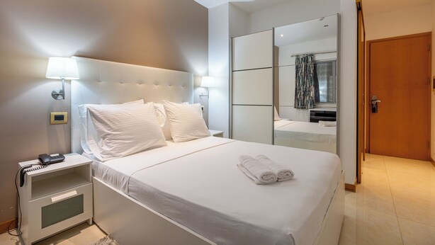 Ett modernt hotellrum med en stor säng, sänglampor, ett nattduksbord, en spegel och en dörr av trä.