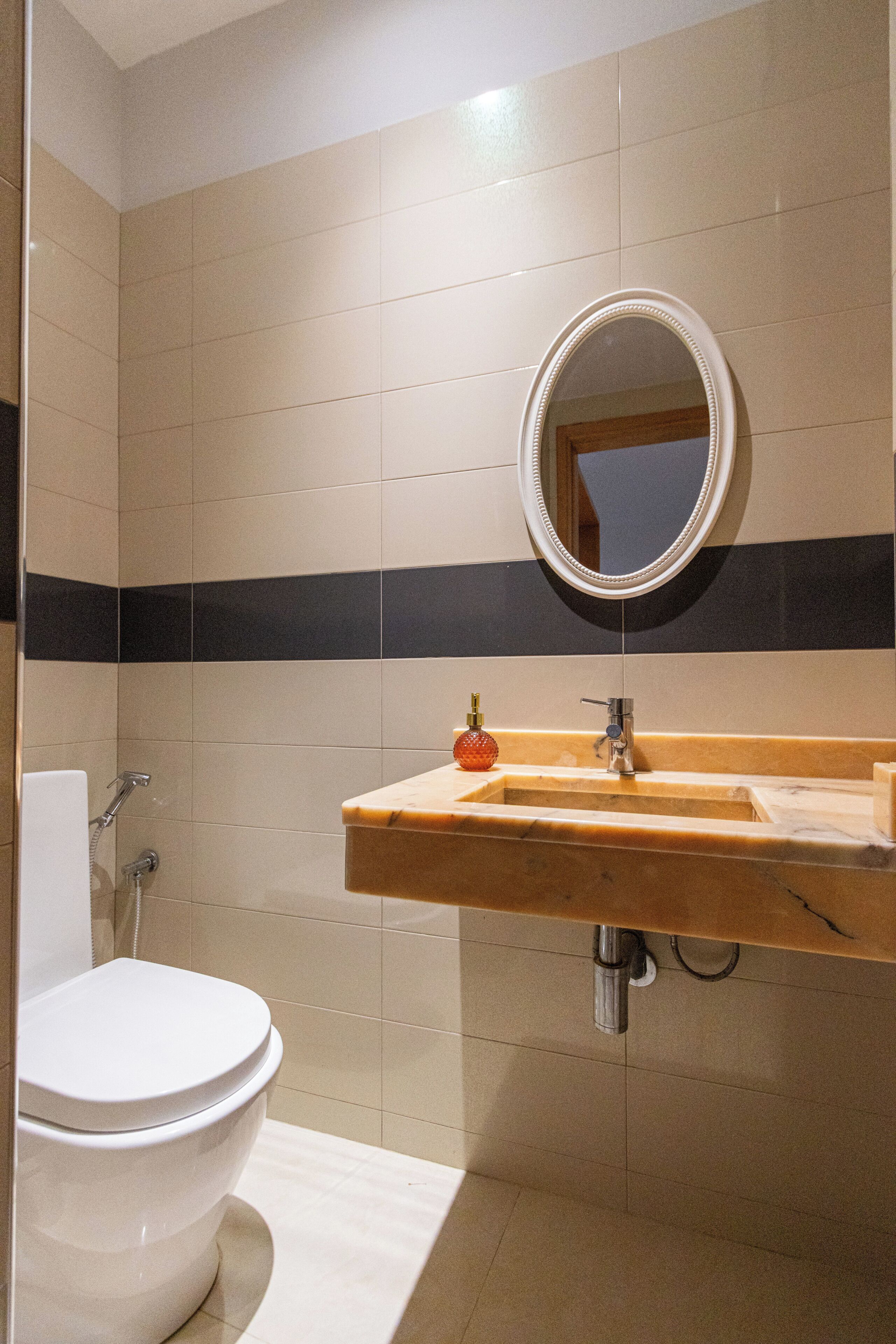Un baño con inodoro, lavabo, espejo y paredes con azulejos.
