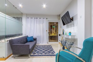 Una sala de estar moderna con un sofá, un sillón azul verdoso, un separador de vidrio, un televisor de pantalla plana y una alfombra estampada.