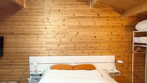 Ein Zimmer mit Holzwänden, einem Bett, einem Nachttisch, einer Lampe und einem Regal mit Handtüchern.