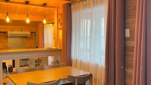 Ein gemütliches Holzinterieur mit einem Esstisch, Stühlen, einer Küchenzeile und einer Wanduhr.
