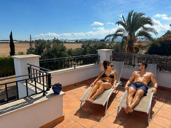 A rooftop terrace with two sun loungers, a potted plant, and a view of the landscape.