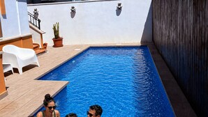 A swimming pool with a tiled edge, a white chair, and a potted plant.