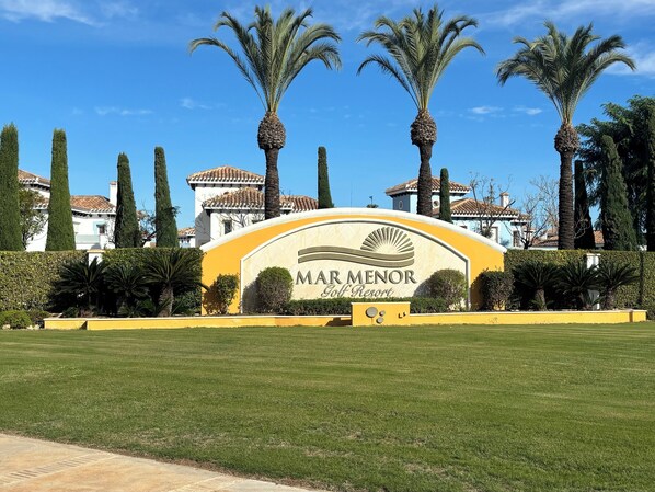 A golf resort sign with palm trees and a building in the background.