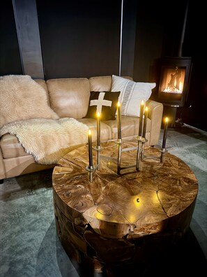 Een gezellige woonkamer met een leren bank, een ronde houten salontafel met kaarsen en een open haard.