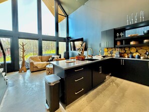 A modern kitchen with a large window, a built-in stove, and a dining area with a sofa. - The Lofts @ Frost Fire- Cabin B (Walhalla)