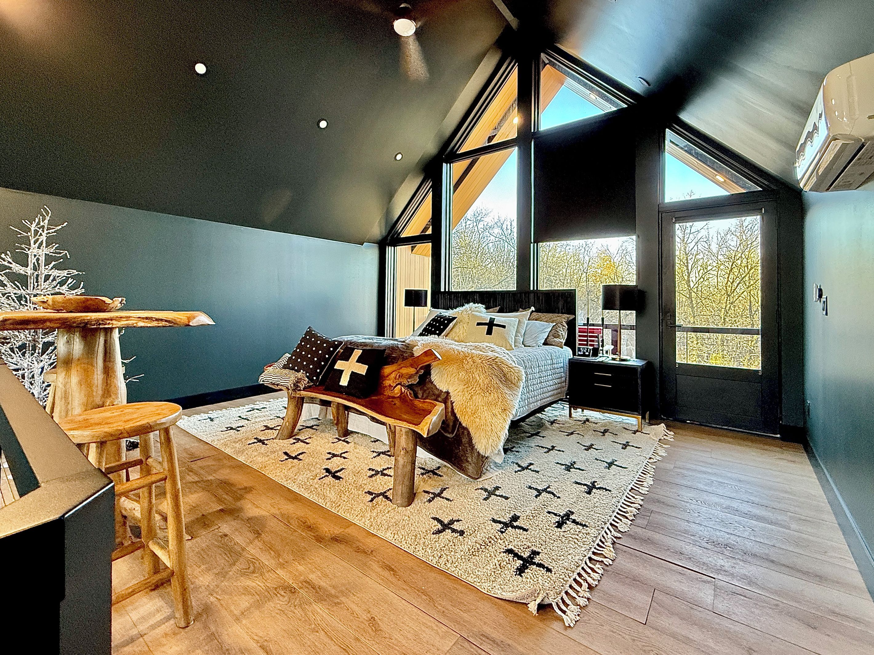A bedroom with a bed, a nightstand, a window, and a view of trees.