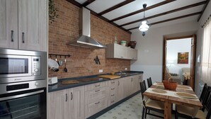 A kitchen with wooden cabinets, a microwave, an oven, a sink, and a dining table with chairs. - El Viejo Olivo Country House - Valencia del Ventoso (Valencia del Ventoso)
