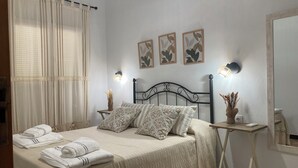 A neatly made bed with a patterned bedspread, two pillows, and folded towels on a bedside table. There are wall-mounted light fixtures and framed artwork above the bed. - El Viejo Olivo Country House - Valencia del Ventoso (Valencia del Ventoso)