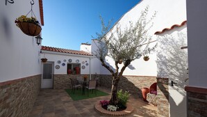A courtyard with a tiled floor, a table with chairs, a hanging flower basket, and a potted tree. - El Viejo Olivo Country House - Valencia del Ventoso (Valencia del Ventoso)