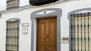 A building with a wooden double door, a balcony with black wrought iron railings, and a sign indicating a rural house. - El Viejo Olivo Country House - Valencia del Ventoso (Valencia del Ventoso)