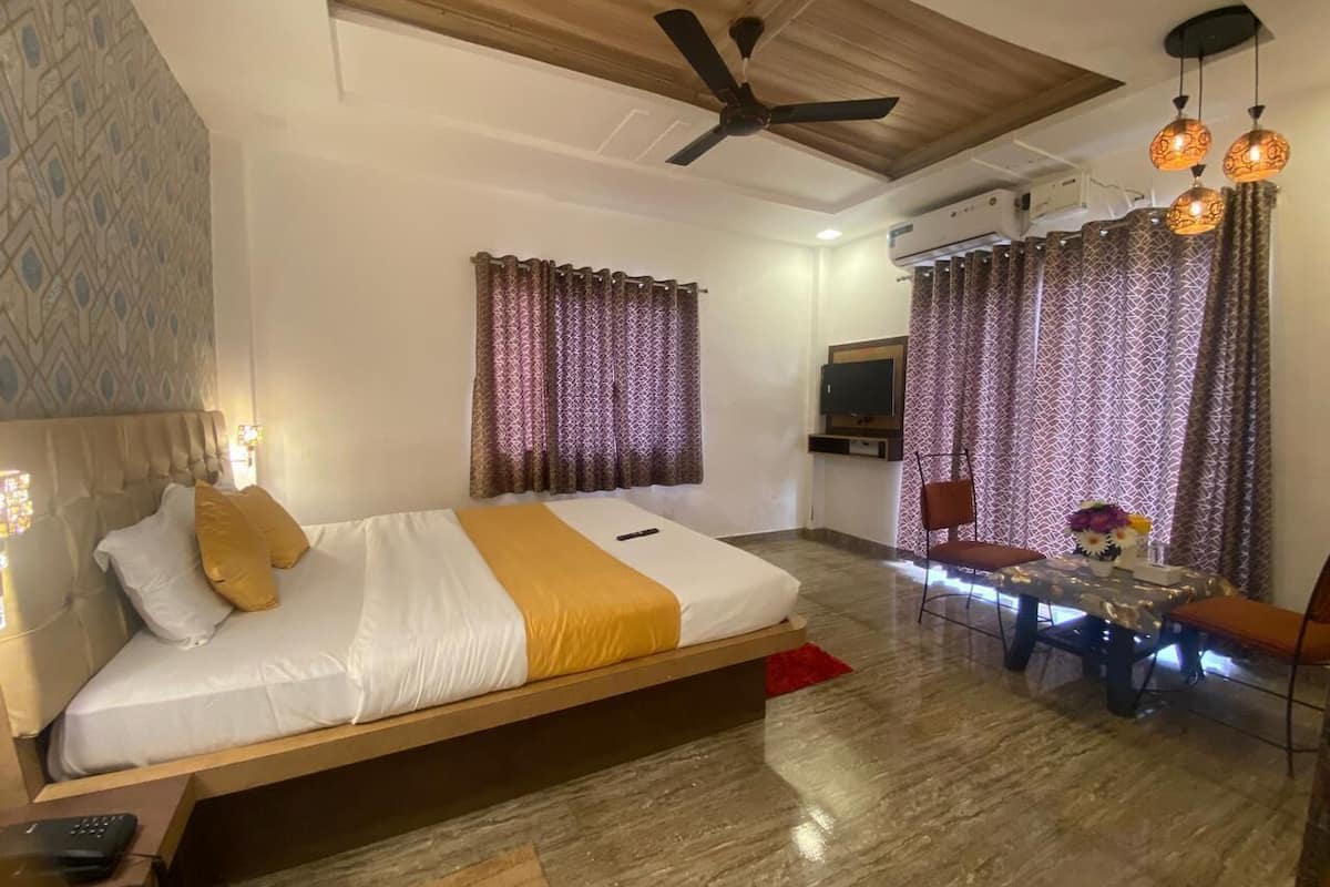 A hotel room with a bed, a dining table, chairs, a ceiling fan, and curtains.