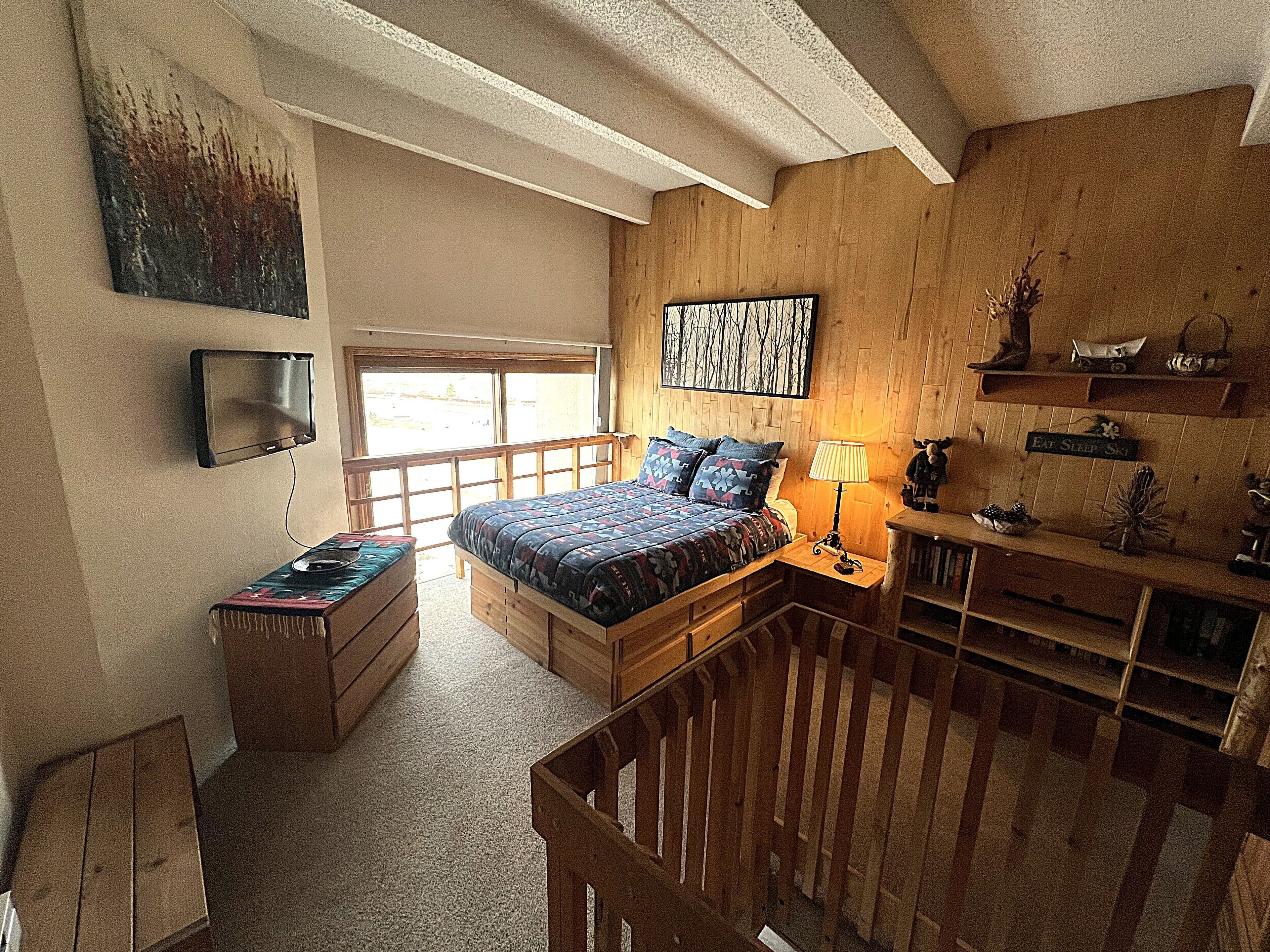 Un dormitorio con cama, escritorio, silla, televisor y ventana.