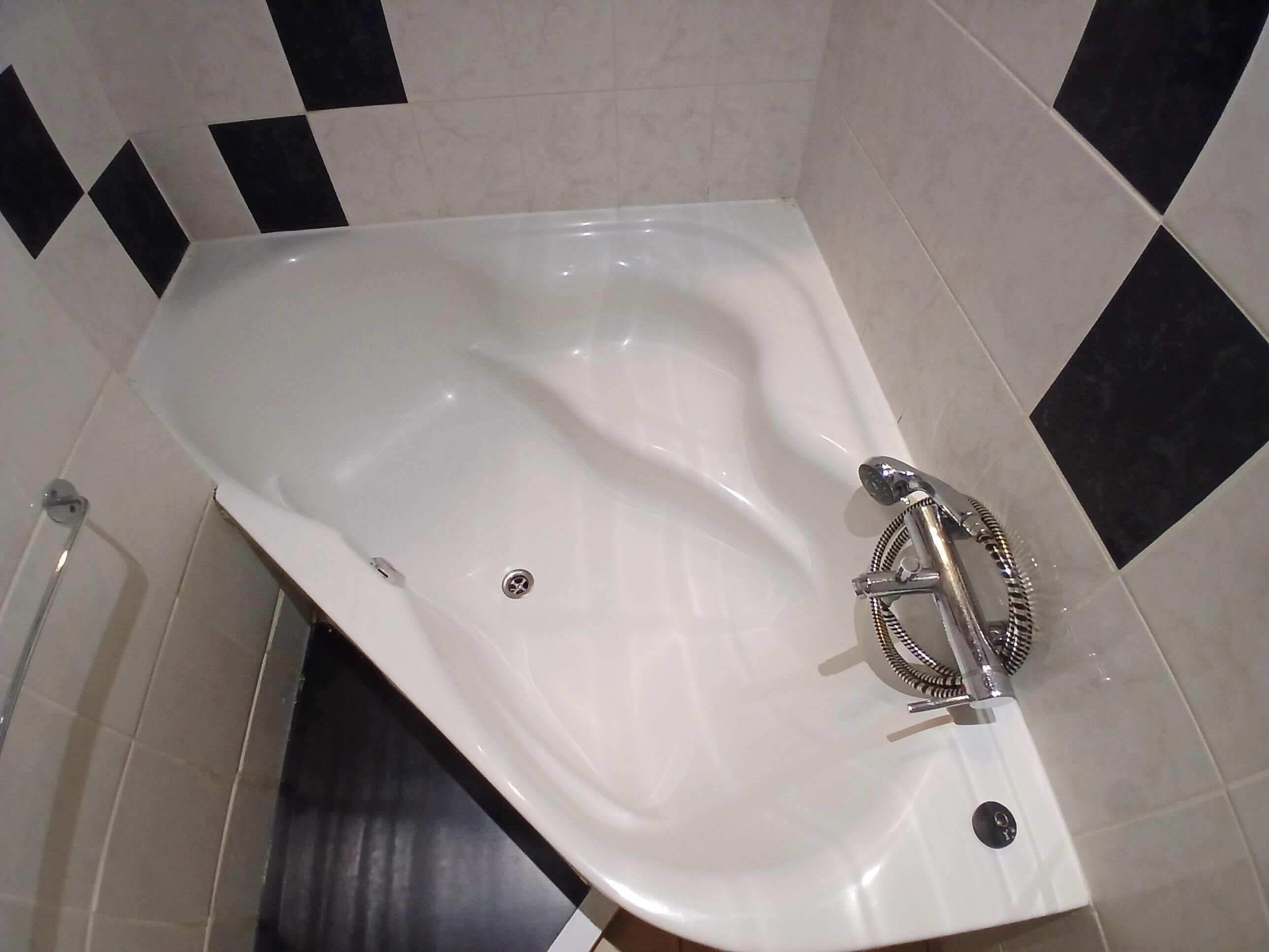 A white bathtub with a handheld showerhead, a drain, and a control knob.
