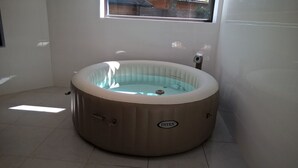 Een bubbelbad in een ruimte met een raam, betegelde vloer en een zichtbare waterpomp.