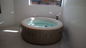 Een bubbelbad in een ruimte met een raam, betegelde vloer en een zichtbare waterpomp.