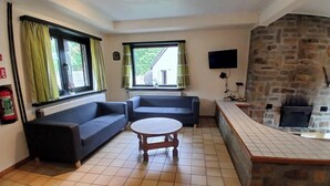 Een woonkamer met twee banken, een ronde tafel, een stenen openhaard en een televisie.