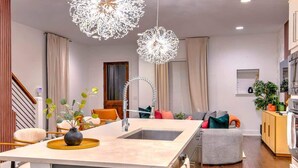 A modern kitchen with a central island, pendant lights, and a dining area with chairs and a table. - Gulch Oasis • 15 Beds • Rooftop Lounge w/ Fire Pit (Nashville)
