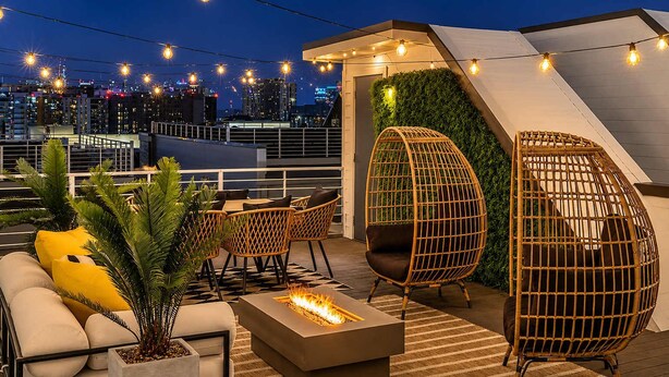 A rooftop terrace with wicker chairs, a fire pit, and a view of the city skyline at night. - Gulch Oasis • 15 Beds • Rooftop Lounge w/ Fire Pit (Nashville)