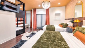 A hotel room with a bunk bed, two single beds, a chandelier, a mirror, and a wooden floor. - Gulch Oasis • 15 Beds • Rooftop Lounge w/ Fire Pit (Nashville)