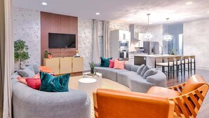 A modern living room with a grey sectional sofa, orange chairs, and a flat-screen TV mounted on the wall. - Gulch Oasis • 15 Beds • Rooftop Lounge w/ Fire Pit (Nashville)