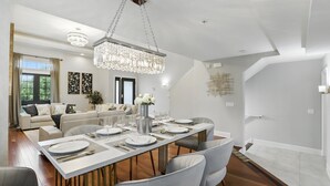 Uma sala de jantar moderna com uma mesa comprida posta para seis pessoas, um candelabro e um sofá ao fundo.