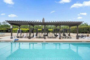 A pool area with a covered seating area, lounge chairs, and a chessboard.